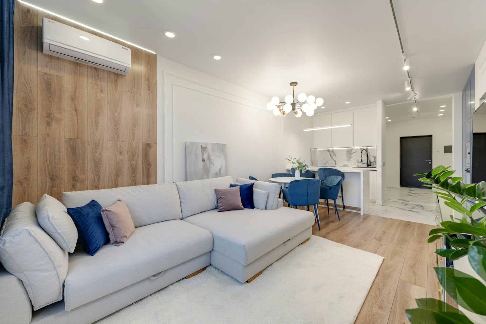 Contemporary living room with stylish furniture, elegant chandelier, and open kitchenette.